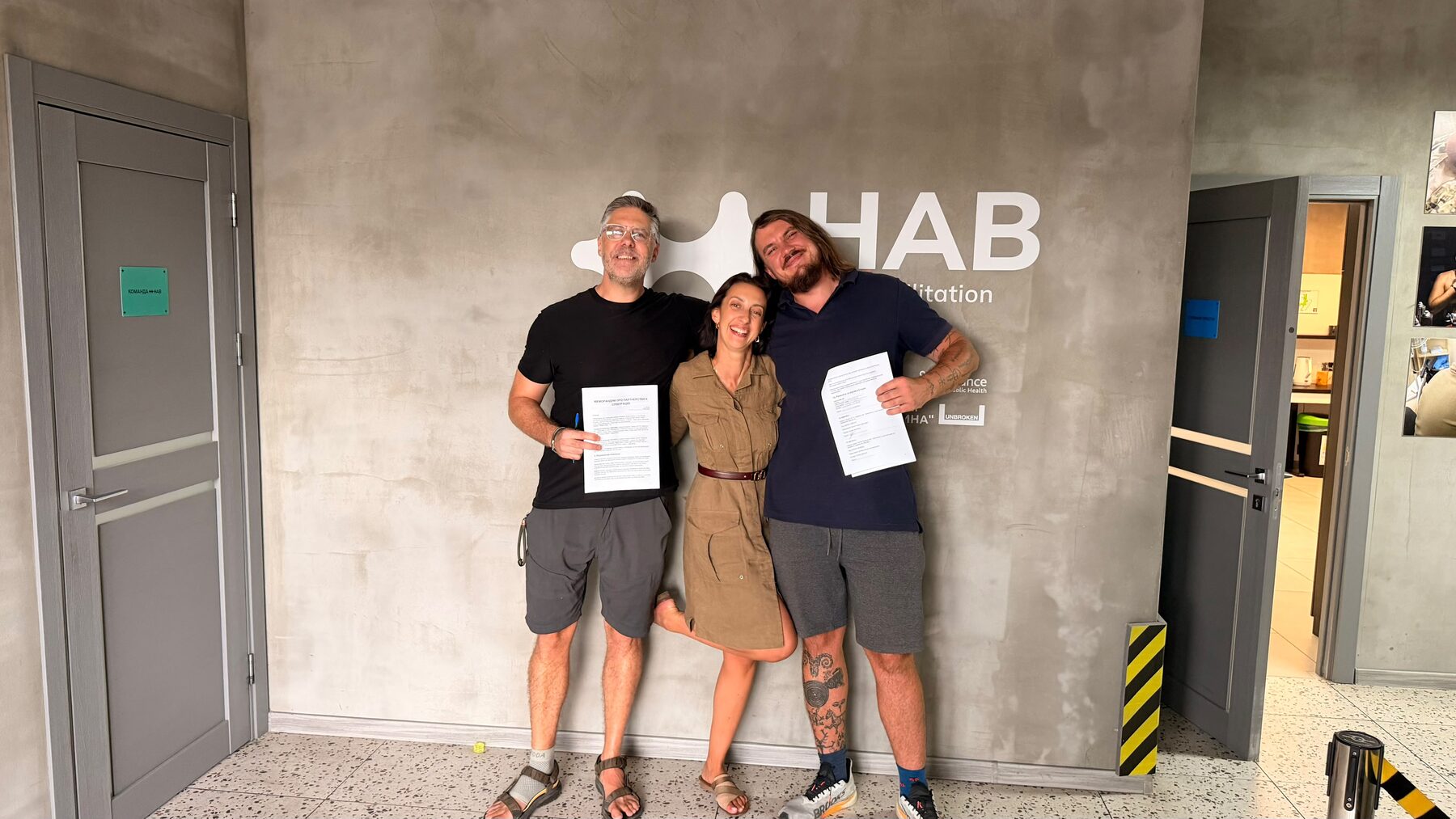 Three people holding partnership documents at HAB rehabilitation