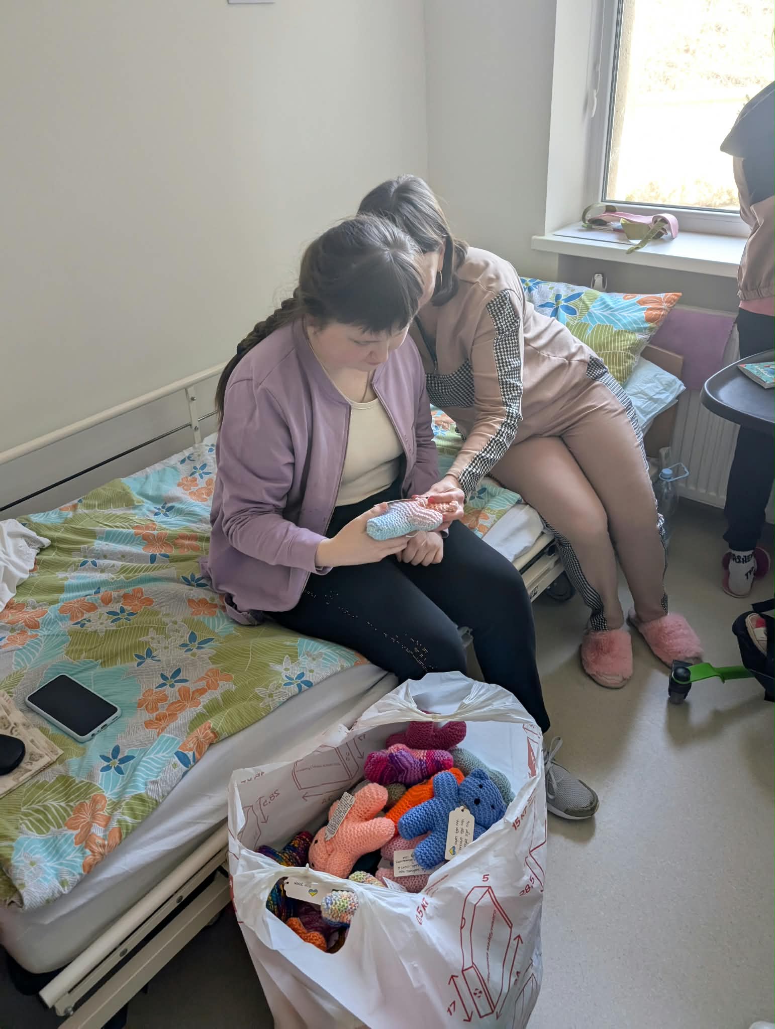 Two people holding handmade knitted toys in a hospital room