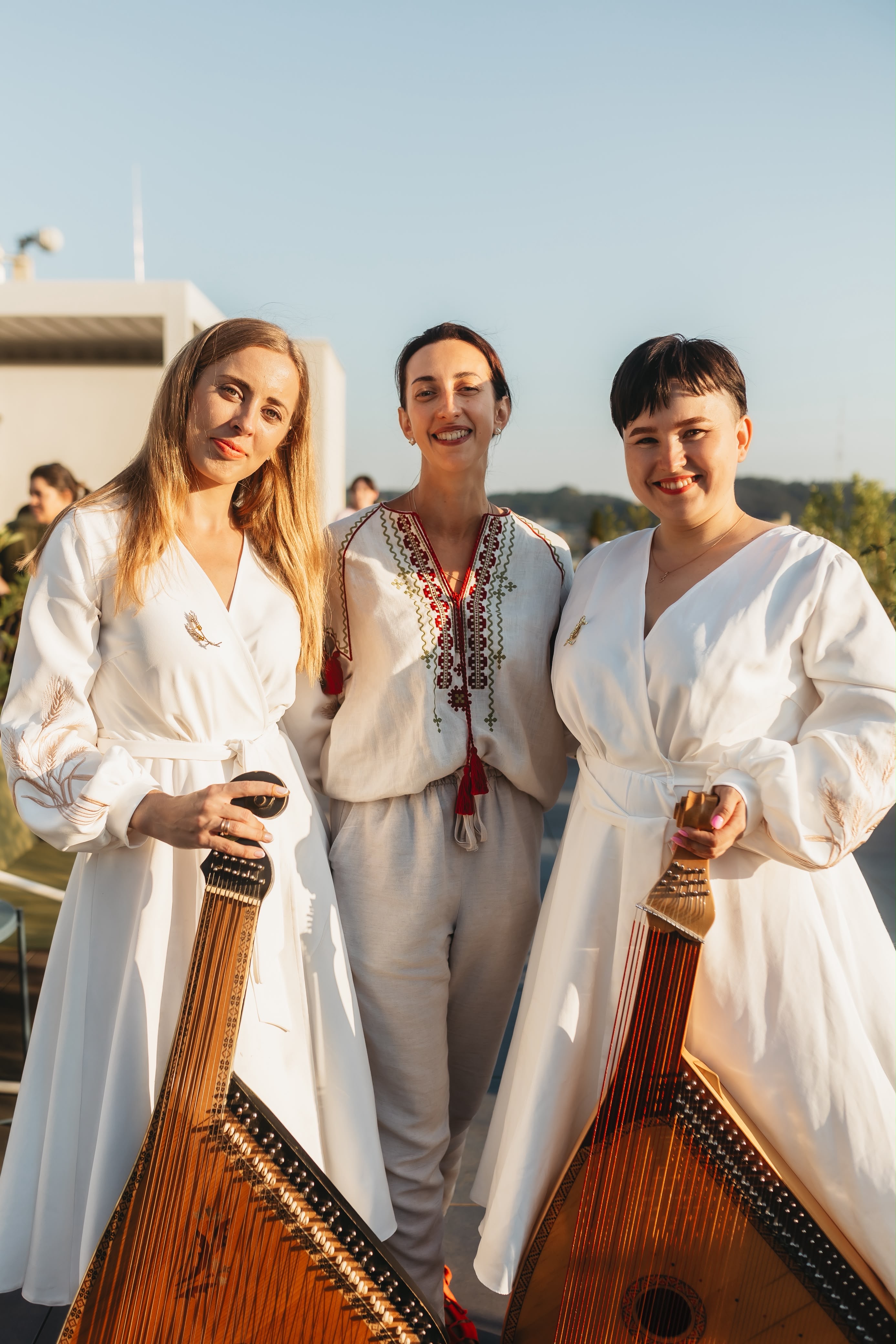 Three women in embroidered Ukrainian clothing standing with banduras at an outdoor event